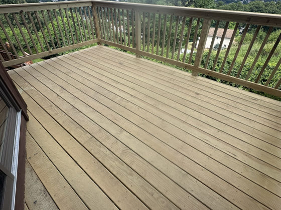 Elevated composite deck with wooden railings overlooking scenic landscape and distant trees