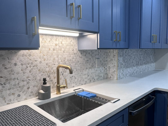 Modern kitchen with blue cabinetry, white countertops, hexagonal tile backsplash, and brass fixtures